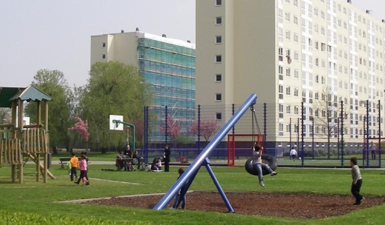 Kinderen spelen in een speeltuin met op de achtergrond een flat