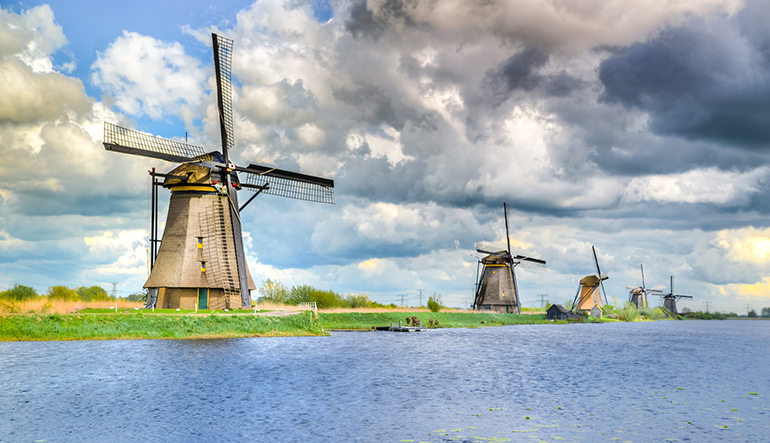 Kinderdijk. Langs de rivier staan vijf molens. Wolkenlucht op de achtergrond