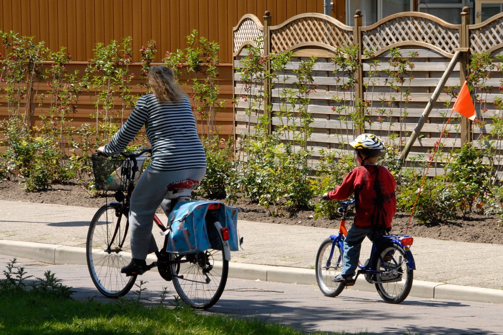 Moeder en kind op de fiets door een straat in een woonwijk