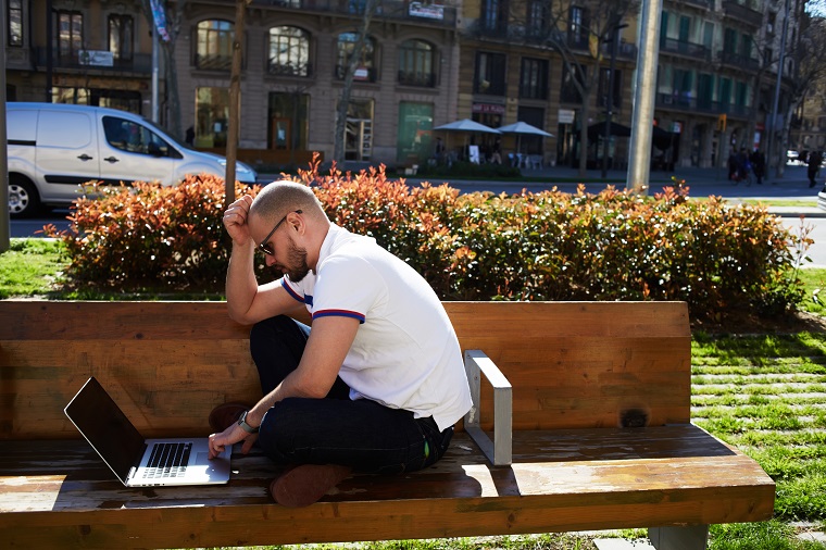 Man werkt op laptop zittend op een bankje in de stad