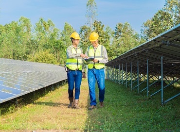 twee werklui met gele helm lopen tussen grondgebonden  zonnepanelen 