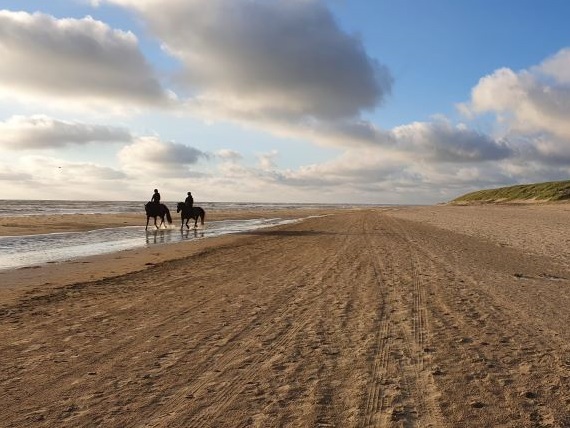 Twee ruiters op een zandstrand met duinen