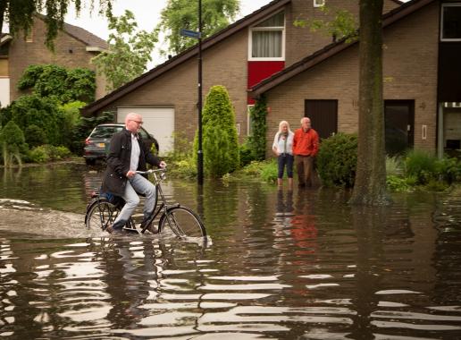 Fietser fietst door straat die onder water staat 