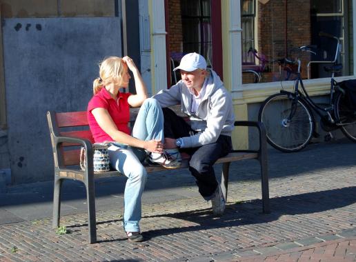 Twee meisjes zitten op bankje in straat te kletsen