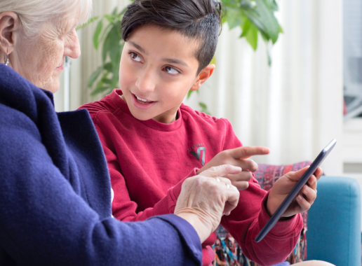 Een jongen die uitleg geef tover een smartphone aan een oudere dame