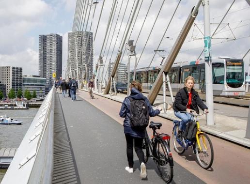 Foto van een brug met een fietser, wandelaar, tram en boten
