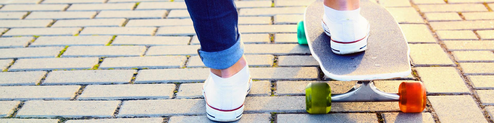 Een skateboard met een oranje en groen wiel, waar iemand met 1 voet op staat
