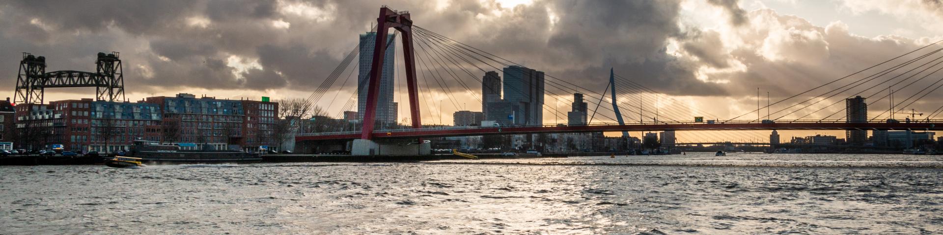 Een foto van de Willemsbrug in Rotterdam, genomen vanaf het water met op de achtergrond de Erasmusbrug