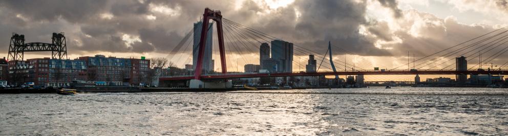 Een foto van de Willemsbrug in Rotterdam, genomen vanaf het water met op de achtergrond de Erasmusbrug