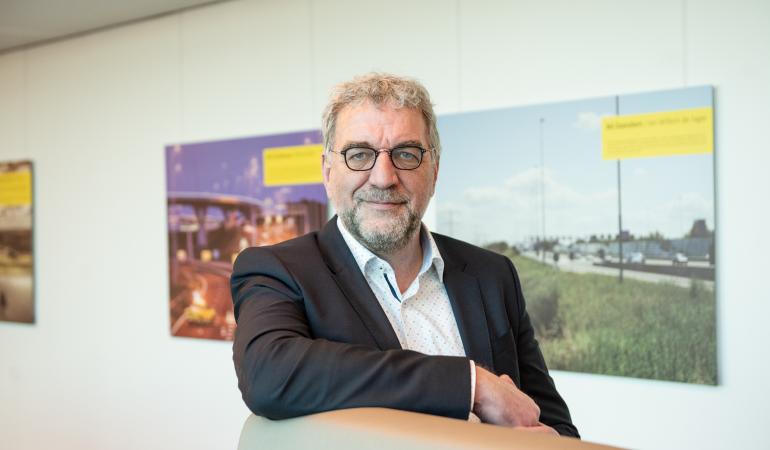 Portretfoto van de heer Ruud Splitthoff aan een hoge tafel met witte achtergrond waar posters hangen