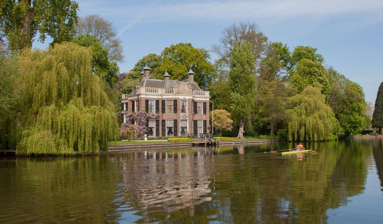 Zicht vanaf het water op een buitenplaats gelegen aan de oever.