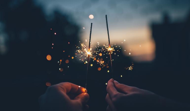 Twee mensen houden vuurwerk sterretjes omhoog tegen een schemer lucht
