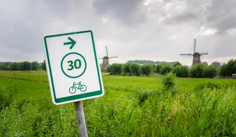 Bord voor fietsers met op achtergrond typisch Nederlands landschap met molens