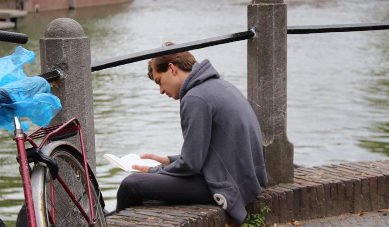 Man leest boek aan gracht