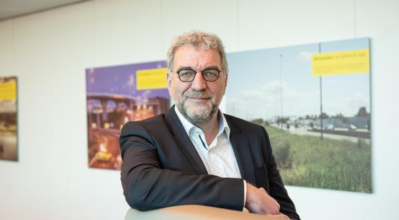 Portretfoto van de heer Ruud Splitthoff aan een hoge tafel met witte achtergrond waar posters hangen