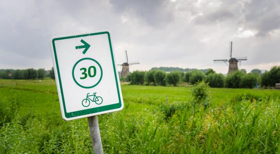 Bord voor fietsers met op achtergrond typisch Nederlands landschap met molens