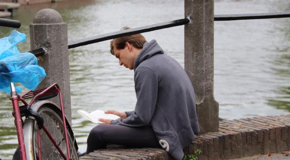 Man leest boek aan gracht